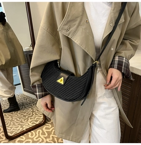 Detail of black woven shoulder bag with golden triangle clasp worn by a model