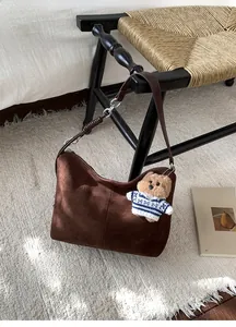 Close-up of deep brown suede tote bag with cute teddy bear charm on textured carpet