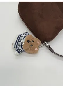 Detail of cute brown plush puppy charm with striped sweater on a suede tote bag