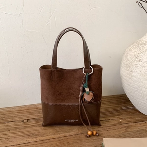Detail of dark brown suede patchwork handbag with leather tassel on a rustic wooden stand