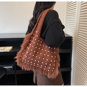 Detail of a brown knit tote bag with pearls and fringe shown on a model shoulder