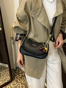 Sac bandoulière élégant en cuir noir avec chaîne dorée et breloque cerise sur un modèle