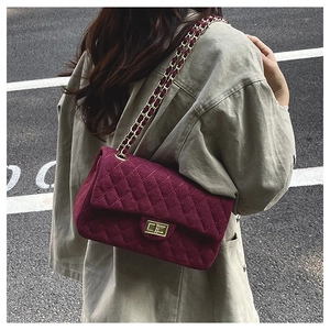 Close-up of burgundy quilted velvet shoulder bag with gold chain strap and square lock