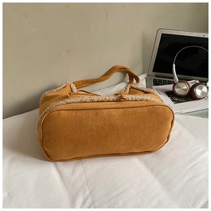 Detail of yellow suede tote bag with beige shearling trim on a desk with a laptop