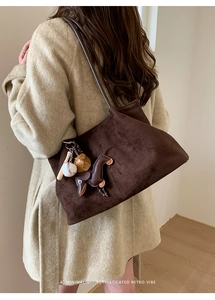 Detail of dark brown suede tote bag with decorative baseball and donkey leather charms