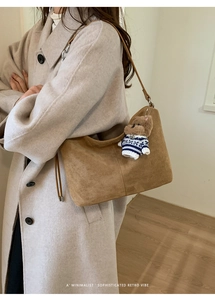 Detail of earthy suede tote bag with stitched texture and a cute brown bear charm