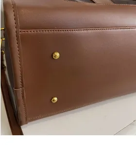 Detail of brown leather bag base with gold metal protective studs and fine stitching