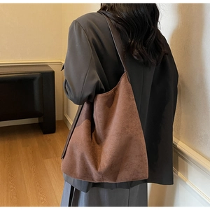 Model wearing a large dark brown suede tote bag with a minimalist shoulder strap style
