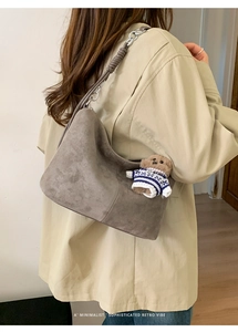 Detail of grey suede hobo bag with metal chain strap and cute bear charm decoration