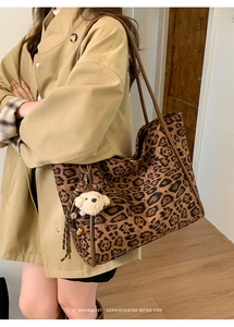 Leopard print tote bag with plush bear charm worn on shoulder over a camel coat