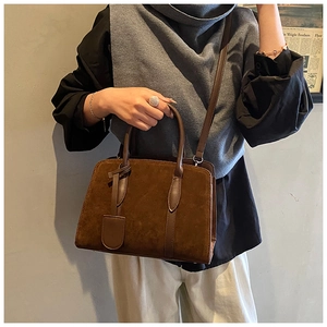 Sac Boston en daim marron foncé porté par un mannequin dans un cadre minimaliste