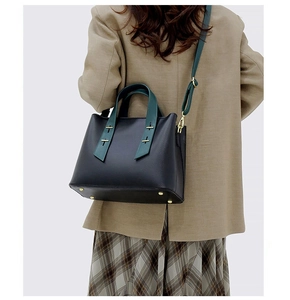 Detailed back view of model carrying a black tote bag with dark green straps and gold hardware