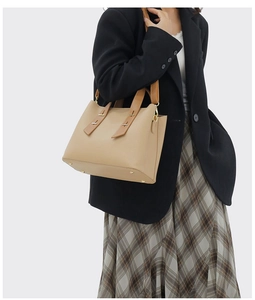 Close-up of beige lychee grain leather tote bag with gold metal handle accents