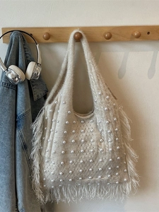 Off-white knit tote bag with pearls and long fringe hanging in a cozy room setting