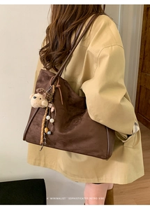 Detailed side view of a brown suede tote bag with a plush bear charm and leather straps