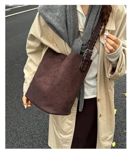 Détail du sac seau en daim marron foncé avec une bandoulière tissée texturée