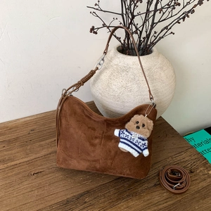 Dark brown suede hobo shoulder bag with cute teddy bear charm on a vintage wooden desk
