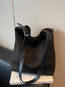 Large black suede tote bag with leather strap placed on books in a minimalist setting