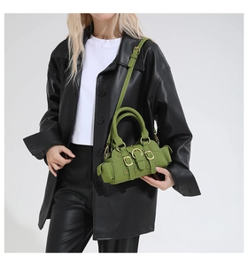 Dettaglio della borsa a tracolla verde minimalista con tasca laterale e fibbie su pelle nera