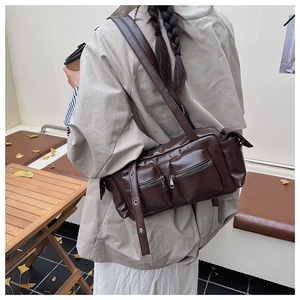 Detail of dark caramel faux leather multi-pocket messenger bag in an autumn street setting