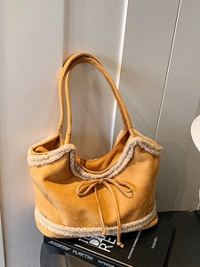 Yellow suede tote bag with faux shearling trim and decorative bow on book stack