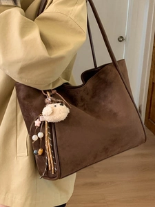 Brown suede tote bag with puppy charm accessory worn by model in trench coat