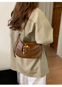 Borsa a tracolla retrò marrone a mezzaluna con nappe di legno in un ambiente minimalista