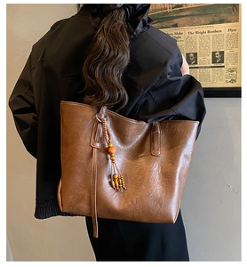 Detailed view of brown tote bag featuring beaded fringe tassels and reinforced stitching