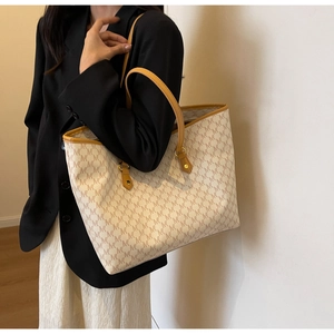Detail of white tote bag featuring brown NY monogram pattern and premium leather handles