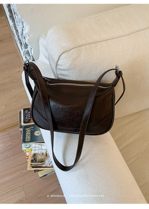 Dettaglio borsa a spalla in pelle marrone scuro con cerniera argentata su divano beige