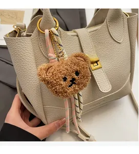 Gros plan d'un charm ours en peluche marron sur un sac seau en cuir crème avec anneau d'or