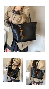 Detail of a large black leather tote bag featuring a yellow gourd and tassel charm