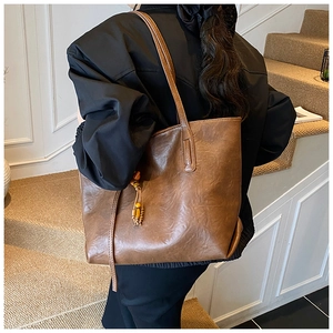 Detail of dark brown tote bag showing textured leather finish and beaded tassel charm