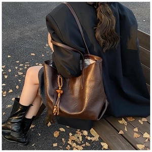 Detail of a large dark brown tote bag with leather tassels and wood beads on a bench