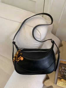 Borsa a mezzaluna nera vintage con ciondolo in legno su un divano bianco