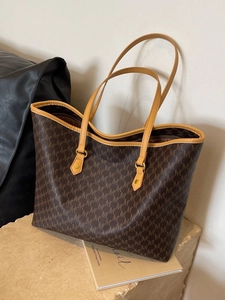 Classic brown tote bag with M-letter monogram print on a minimalist stone pedestal