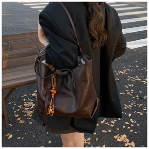 Detail of dark brown tote bag with retro tassel charm in an autumn outdoor park setting