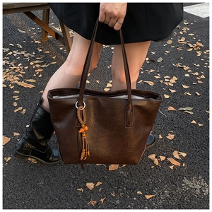 Detail of dark brown faux leather tote bag with wooden bead tassel on autumn background