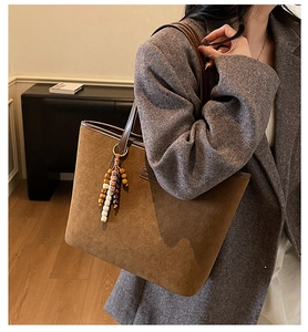 Detailed texture of brown suede tote bag featuring a leather handle and a tassel charm