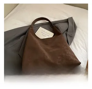 Détail d'un sac cabas en daim marron foncé avec logo doré et un design minimaliste