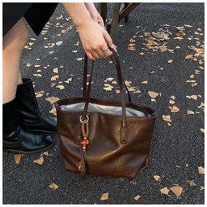 Close-up of a brown tote bag featuring a woven tassel detail against fallen autumn leaves