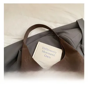 Détail du sac hobo en daim marron foncé sur fond de blazer gris avec poignée