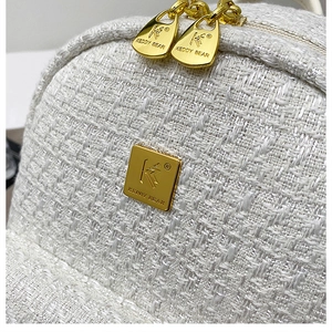 Detail of white tweed fabric texture with gold double zippers and brand logo plate