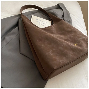 Close-up of deep brown suede tote bag featuring a small gold logo on gray suiting