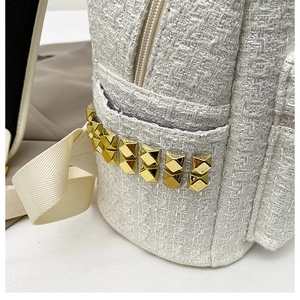 Detail of white tweed backpack featuring golden square rivets and woven texture