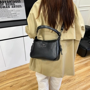 Detailed back view of a minimalist black shiny leather crossbody bag styled with a beige coat