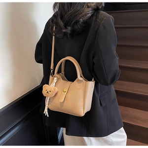Détail du sac seau beige à motif litchi avec pendentif ours et foulard sur un mannequin