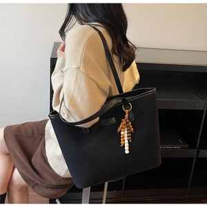 Détail du sac cabas en daim noir avec pompons en perles de bois colorées sur un mannequin