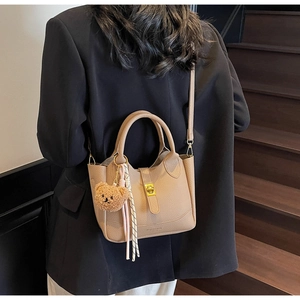 Détail d'un sac seau en cuir beige avec pendentif ours et foulard en soie sur la bandoulière