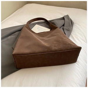 Detailed shot of brown suede tote bag on a white bed with a grey blazer background